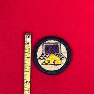May include: A blue and white embroidered Boy Scout patch with a computer screen, a checkered floor, and a yellow construction hat with the letters "J.E." on it.
