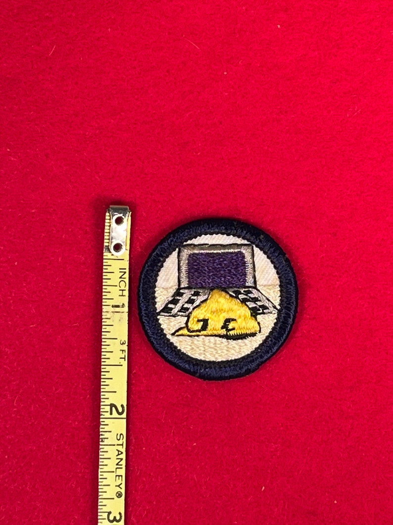 May include: A blue and white embroidered Boy Scout patch with a computer screen, a checkered floor, and a yellow construction hat with the letters "J.E." on it.
