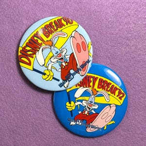 May include: Two round Disney Break pins featuring Roger Rabbit. One pin is light blue with "Disney Break 90" text, and the other is dark blue with "Disney Break 92". Both pins have Roger Rabbit holding a yellow sign.
