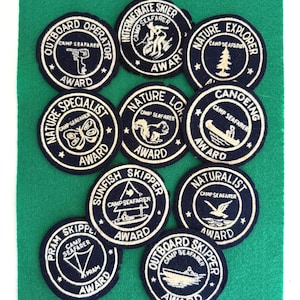 May include: A white ceramic mug with a black handle and the text "But First, Coffee" in a black, handwritten-style font. The mug is on a white surface.