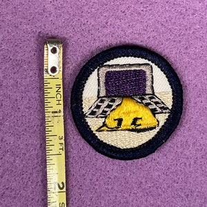 Puede incluir: Una insignia de m&eacute;rito de Boy Scout bordada en azul y blanco con un casco amarillo y una pantalla de computadora morada. La insignia dice "15".