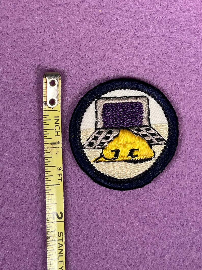 Puede incluir: Una insignia de m&eacute;rito de Boy Scout bordada en azul y blanco con un casco amarillo y una pantalla de computadora morada. La insignia dice "15".