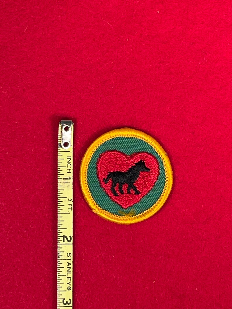 May include: A green and red embroidered patch with a black horse inside a heart. The patch is surrounded by a yellow border.