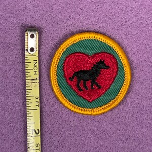 Puede incluir: Un parche bordado verde y rojo con una silueta negra de un caballo dentro de un coraz&oacute;n rojo. El parche est&aacute; rodeado por un borde amarillo.