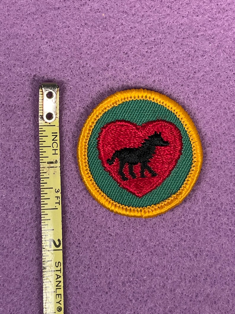 Puede incluir: Un parche bordado verde y rojo con una silueta negra de un caballo dentro de un coraz&oacute;n rojo. El parche est&aacute; rodeado por un borde amarillo.