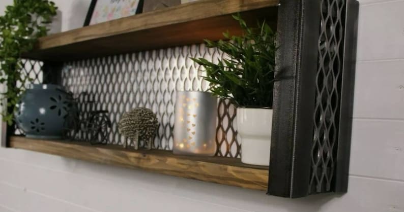 May include: A wooden shelf with two tiers, featuring a black metal frame with a diamond pattern. The shelf is decorated with a silver metallic tile backsplash and has various decorative items, including a blue ceramic vase, a silver candle holder, and a small metal sculpture.