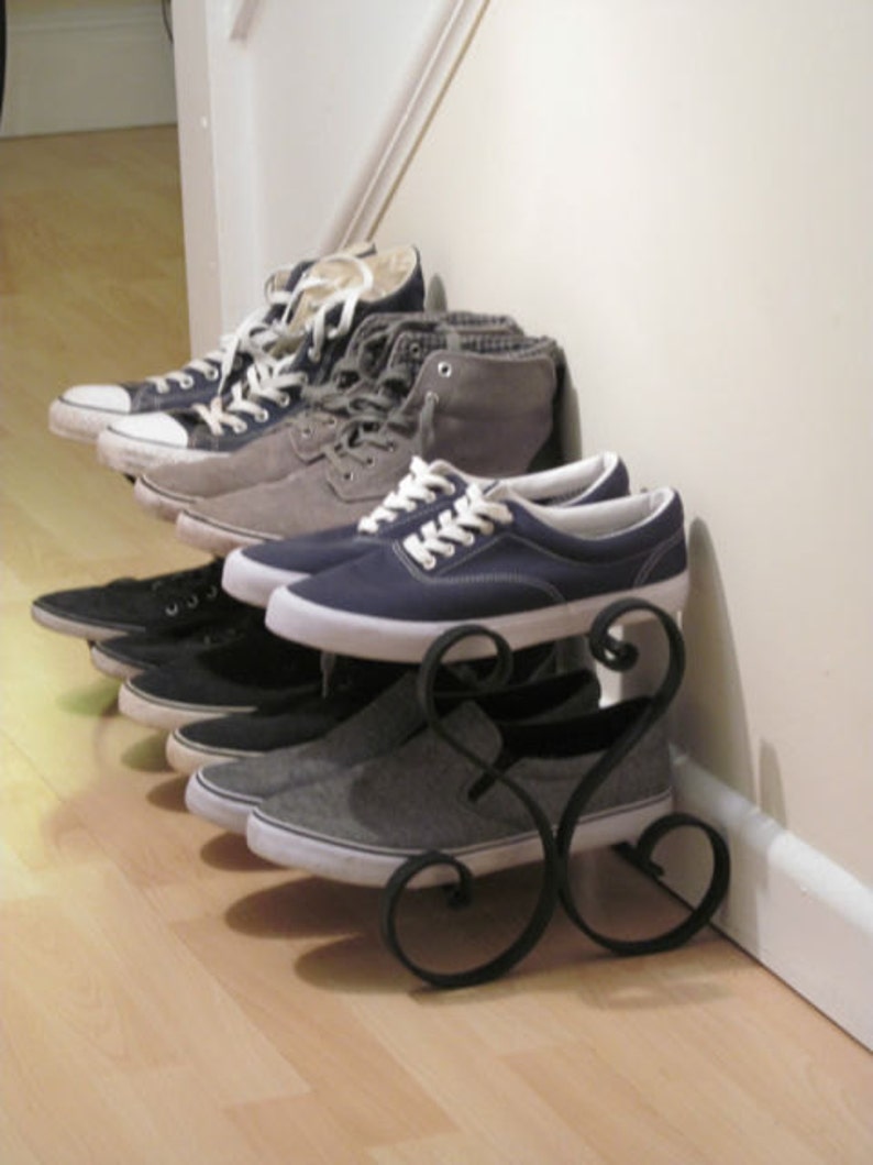 May include: A black metal shoe rack with five pairs of shoes on it. The shoes are a mix of black, grey, and blue canvas sneakers.