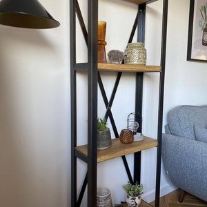 May include: A black metal shelf unit with four wooden shelves. The shelves are decorated with plants, vases, and other decorative items.