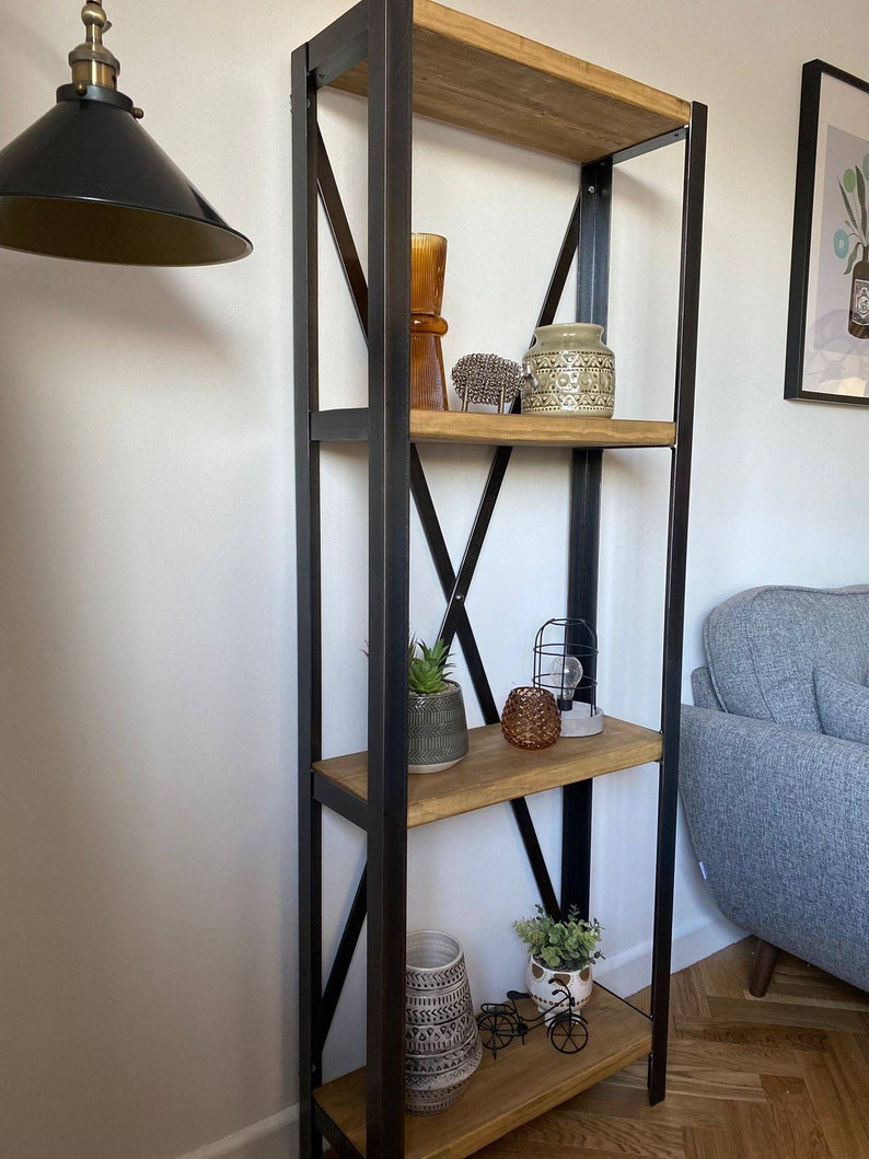 May include: A black metal shelf unit with four wooden shelves. The shelves are decorated with plants, vases, and other decorative items.