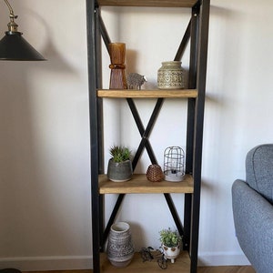 May include: A black metal shelf unit with four wooden shelves. The shelves are decorated with various items, including a vase, a potted plant, a small lamp, and a few decorative objects.