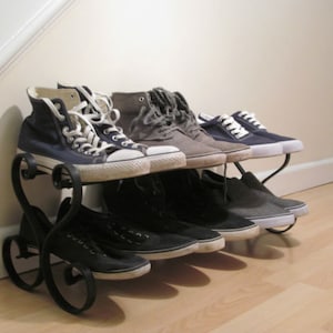 May include: A black metal shoe rack with a heart-shaped design holds a variety of trainers, including blue canvas high-tops, grey canvas low-tops, and black canvas low-tops.
