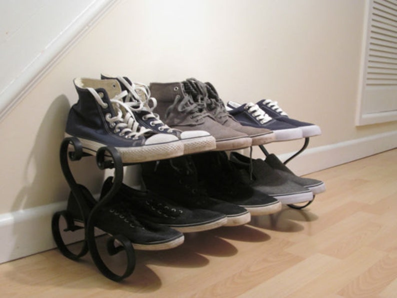 May include: A black metal shoe rack with a heart-shaped design holds a variety of trainers, including blue canvas high-tops, grey canvas low-tops, and black canvas low-tops.
