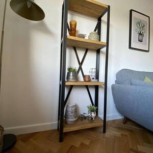 May include: A black metal and wood bookshelf with four shelves. The shelves are filled with decorative items, including a vase, a birdcage, and plants. The bookshelf is standing on a wood floor.