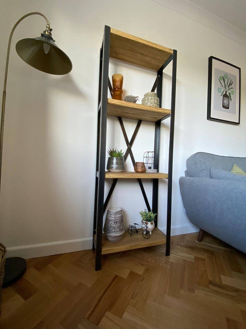 May include: A black metal and wood bookshelf with four shelves. The shelves are filled with decorative items, including a vase, a birdcage, and plants. The bookshelf is standing on a wood floor.