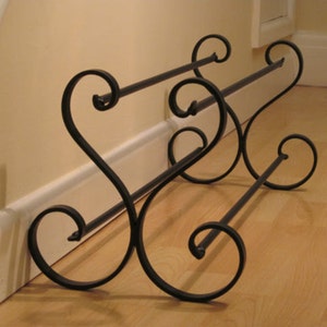 May include: Black metal shoe rack with a decorative scroll design. The rack has two tiers and is designed to be placed against a wall.