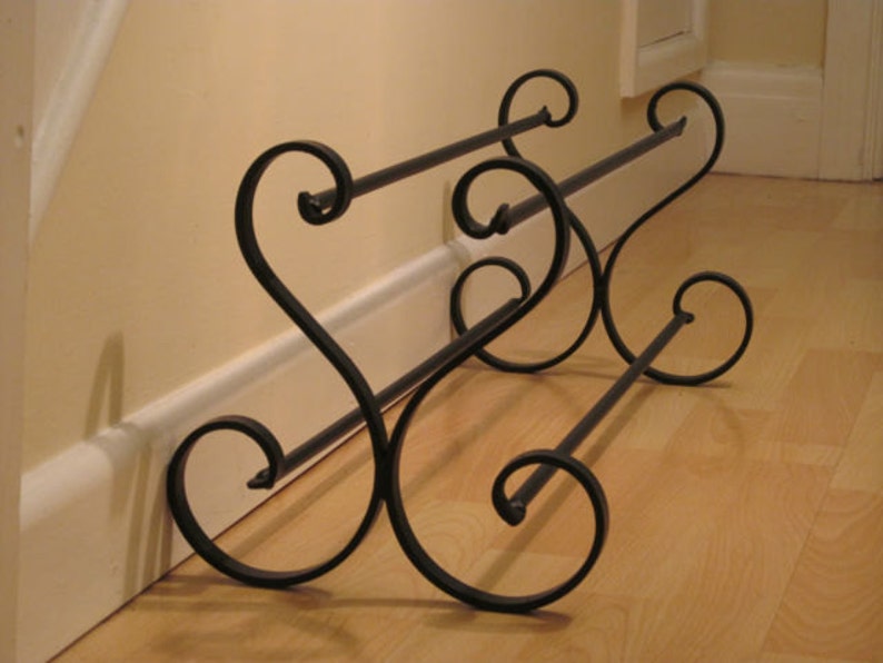 May include: Black metal shoe rack with a decorative scroll design. The rack has two tiers and is designed to be placed against a wall.