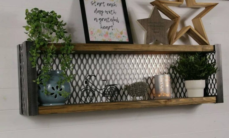 May include: A rustic wooden shelf with metal accents features a silver mesh backing. The shelf is decorated with a framed print that reads "Start each day with a grateful heart."  There are also two wooden stars, a small metal bicycle, a ceramic pot with a green plant, a silver candle holder, and a small ceramic pot with a green plant.