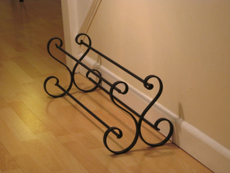 May include: A black metal shoe rack with two tiers and decorative scrollwork. The rack is designed to hold shoes and is placed against a wall.