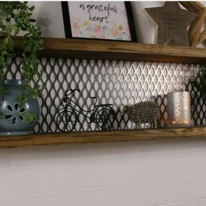 May include: A two-tiered wooden shelf with metal accents and a wire mesh back. The shelf is decorated with plants, a small bicycle figurine, and a silver metal sheep figurine. The top shelf has a framed print with the text "a grateful heart".