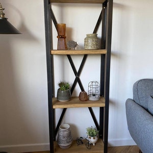 May include: A four-tier wooden shelf unit with black metal frame and criss-cross accents. The shelves are decorated with a variety of items, including a brown glass vase, a ceramic vase with a geometric pattern, a small potted succulent, a caged light fixture, a woven basket, and a small potted plant.