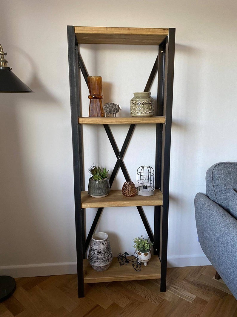 May include: A four-tier wooden shelf unit with black metal frame and criss-cross accents. The shelves are decorated with a variety of items, including a brown glass vase, a ceramic vase with a geometric pattern, a small potted succulent, a caged light fixture, a woven basket, and a small potted plant.