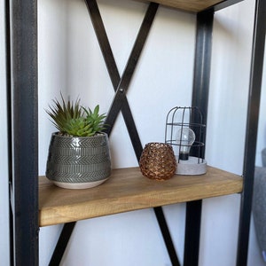 May include: A black metal shelf unit with wooden shelves. The top shelf has a potted succulent plant, a decorative candle holder, and a caged light bulb.