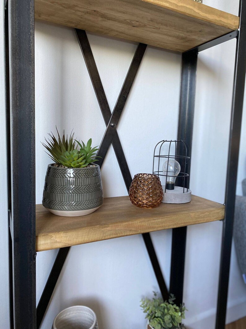 May include: A black metal shelf unit with wooden shelves. The top shelf has a potted succulent plant, a decorative candle holder, and a caged light bulb.