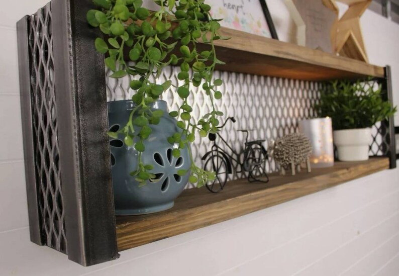 May include: Two-tiered metal and wood shelf with a geometric pattern on the front. The shelf is decorated with a blue ceramic planter with a plant, two small metal bicycles, and a silver metal sheep. The shelf is mounted on a white wall.
