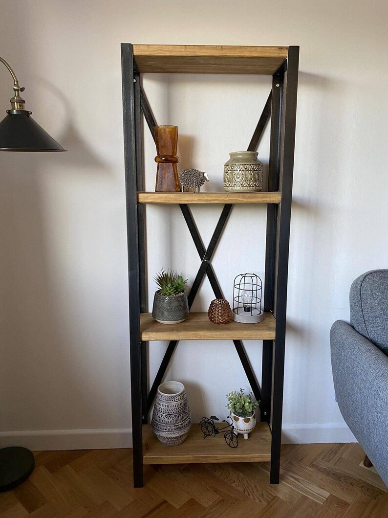 May include: A black metal shelf unit with four wooden shelves. The shelves are decorated with various items, including vases, plants, and decorative objects. The shelf unit is standing on a wooden floor.