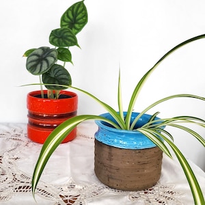 Puede incluir: Un juego de tres tazas de cerámica con un acabado moteado y mate. Cada taza presenta un color diferente: azul claro, crema y gris. Las tazas tienen un diseño simple y moderno y un asa cómoda.