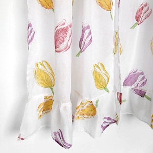 May include: White sheer curtain panels adorned with a repeating pattern of colorful tulip illustrations. The tulips feature yellow, purple, and pink petals with green stems. The bottom edge has a ruffled trim.