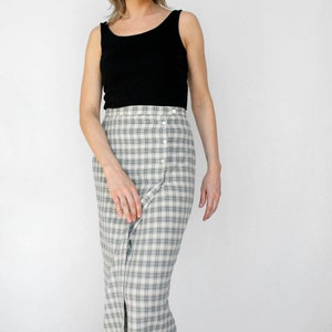 Può includere: Un top nero senza maniche abbinato a una gonna a quadri a vita alta con bottoni, nei toni del grigio e del bianco. La gonna ha uno spacco frontale e una vestibilità su misura, creando un outfit classico e versatile.