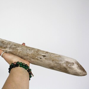 May include: A weathered, light brown piece of driftwood, held against a white background. The wood has a natural, textured surface with variations in color. The driftwood is a long, cylindrical shape, perfect for home decor or craft projects.