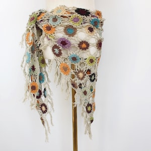 May include: A triangular crochet shawl made of beige yarn featuring a pattern of interconnected circular motifs in various colors including orange, blue, purple, brown, and yellow, finished with long fringe along the edges of the garment.
