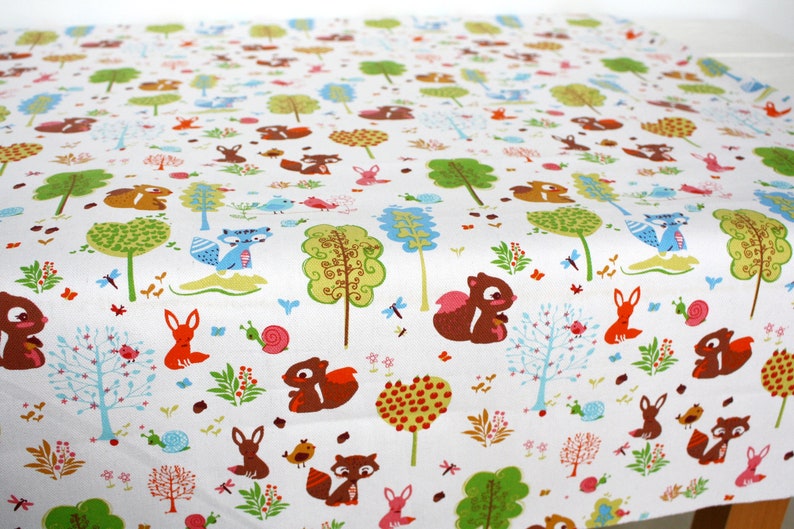May include: A white fabric featuring a repeating pattern of brown squirrels, orange foxes, blue raccoons, pink snails, and various stylized green and blue trees. The design includes small red berries, tiny flowers, and dragonflies scattered throughout.
