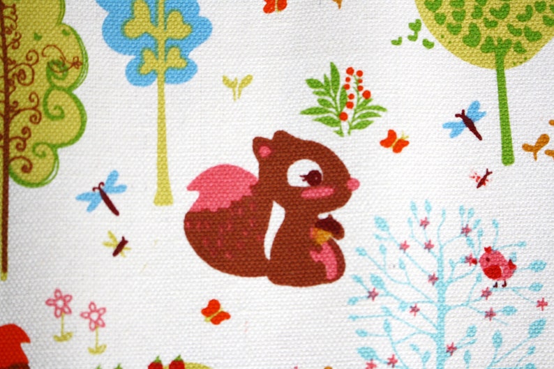 May include: A white fabric featuring a repeating pattern of a brown squirrel holding an acorn, surrounded by colorful trees in shades of green and blue, small pink flowers, orange butterflies, blue dragonflies, and a small red bird on a branch.
