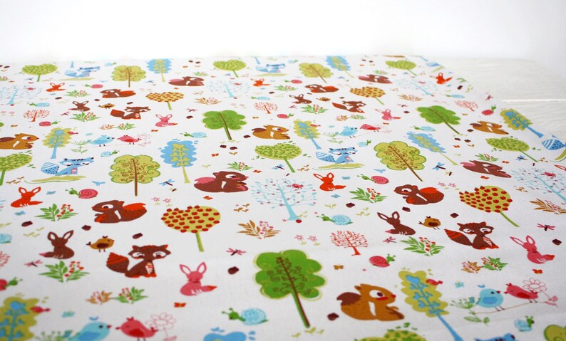 May include: A white fabric featuring a repeating pattern of colorful woodland elements including brown squirrels, orange foxes, blue birds, green trees, pink snails, and small floral motifs scattered across the surface in a dense, illustrative design.