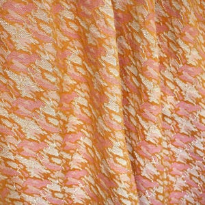 May include: A fabric featuring a textured, woven pattern in shades of golden yellow, soft pink, and off-white. The material displays a repeating, abstract, organic design with a slight sheen, characterized by gathered folds that create depth and shadow.
