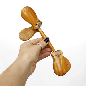 May include: Wooden castanets with a light brown finish. The castanets are held together with twine and have a guitar-shaped design. The image shows the castanets against a white background.