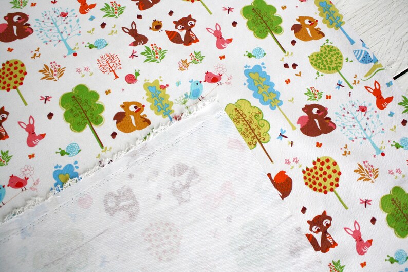 May include: A white fabric featuring a repeating pattern of colorful woodland animals including squirrels, rabbits, and birds, interspersed with stylized green and blue trees, small snails, and floral elements, with a frayed edge showing the reverse side.