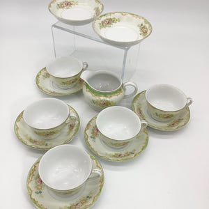 May include: A set of vintage teacups and saucers with a floral pattern in shades of pink, green, and gold. The set includes a creamer and two small bowls.