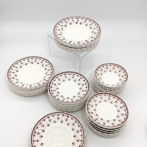 May include: A set of white ceramic plates with a brown floral pattern. The plates are stacked in groups of different sizes.