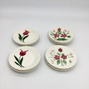 May include: Four small, off-white ceramic plates with scalloped edges. Two stacks feature a red tulip design with green leaves, while the other two have a floral arrangement with red and pink flowers and green leaves.