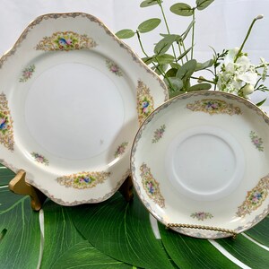 Op de afbeelding: Een witte porseleinen bord- en schotelset met gouden rand en bloemaccenten. Het bord is vierkant met geschulpte randen en de schotel is rond. Beide stukken hebben een decoratieve rand met vogels en bloemen.
