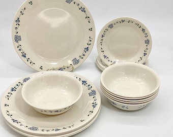 Pode incluir: Um conjunto de jantar creme com pratos e tigelas. Os pratos e tigelas são decorados com um padrão floral azul nas bordas. O conjunto inclui pratos de jantar, pratos de salada e tigelas, perfeitos para servir refeições.