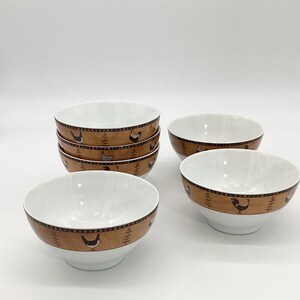 May include: Set of six white ceramic bowls with a brown and orange border featuring a repeating pattern of chickens and plants.