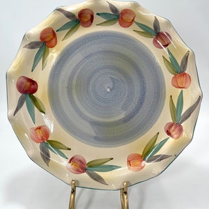 May include: A ceramic serving plate with a scalloped edge and a blue and white swirl design. The plate is decorated with a border of painted peach-colored fruit and green leaves.