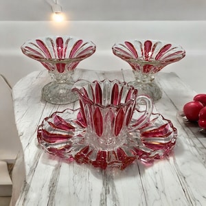 May include: A set of three vintage glass serving dishes with a red and clear design. The dishes are in the shape of a flower with a scalloped edge. The set includes two bowls and a creamer.