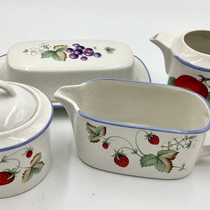 May include: A set of four ceramic serving dishes with a white background and a blue trim. The dishes feature a floral design with strawberries, grapes, and leaves.