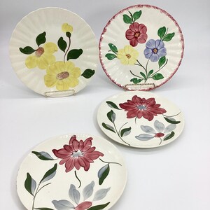 May include: Four vintage floral patterned dinner plates. The plates have a white background with hand-painted flowers in shades of yellow, red, blue, and green.